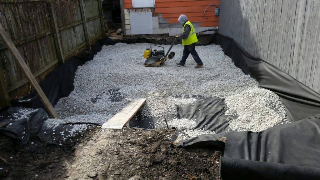Crew compacting a crushed stone base over fabric for permeable pavers
