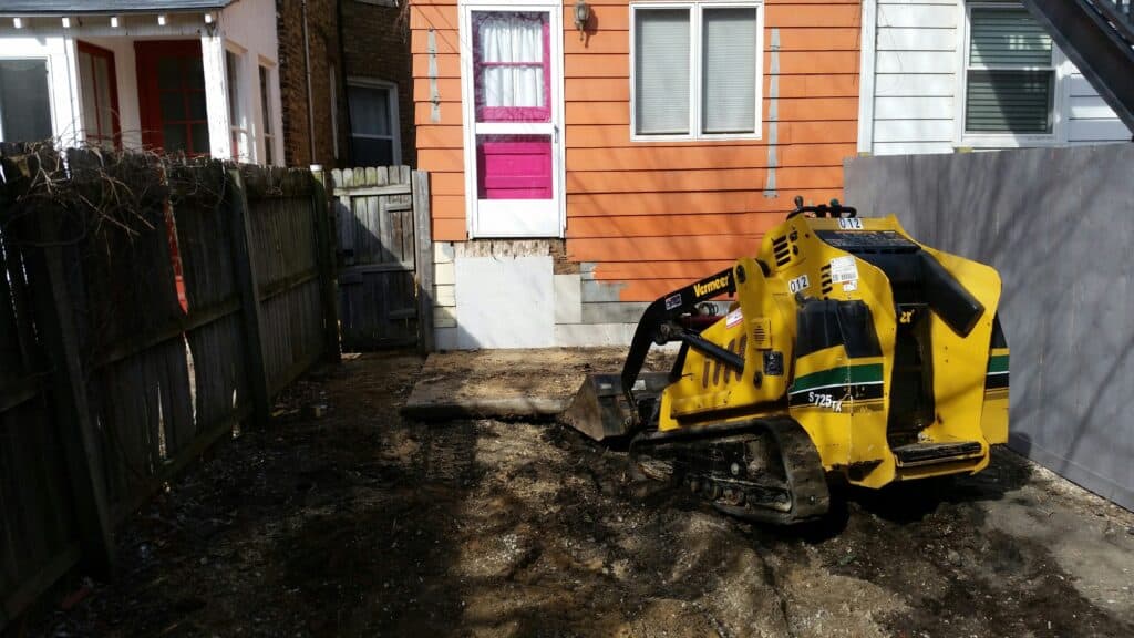 Compact track loader digging out a narrow city backyard for a paver patio