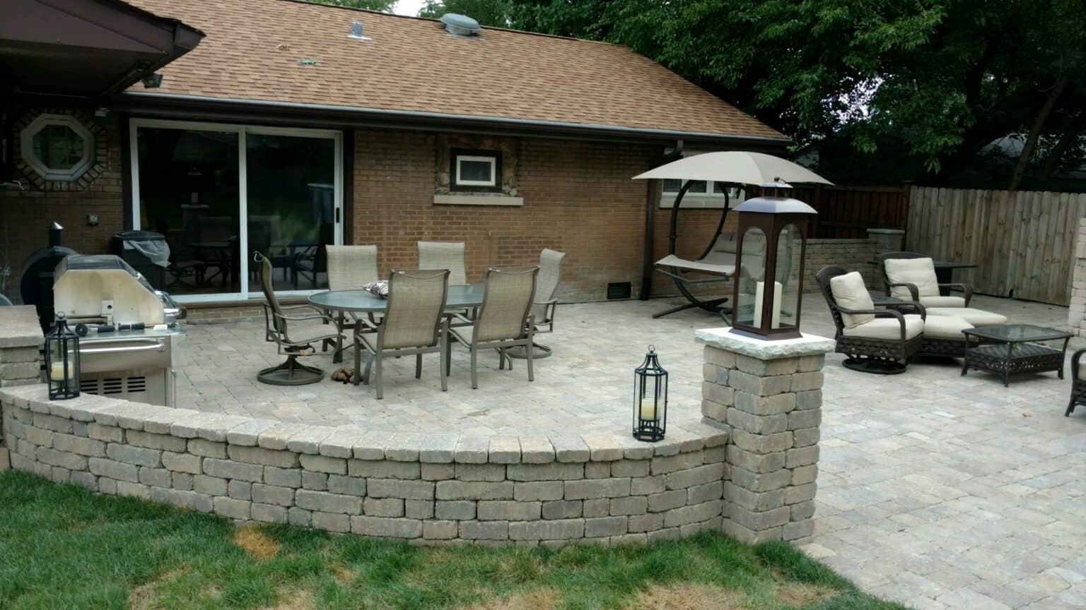Finished paver patio with a curved seat wall and outdoor furniture behind a brick ranch home