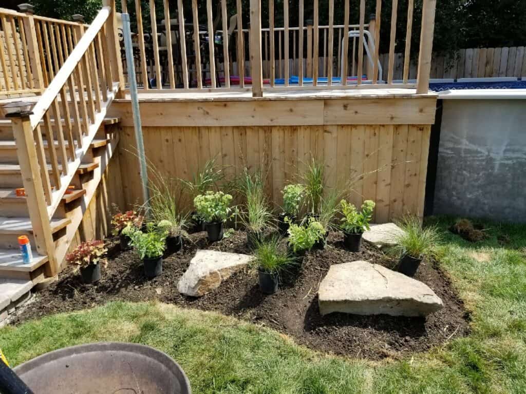 New planting bed with ornamental grasses, perennials and stone boulders going in beside a deck