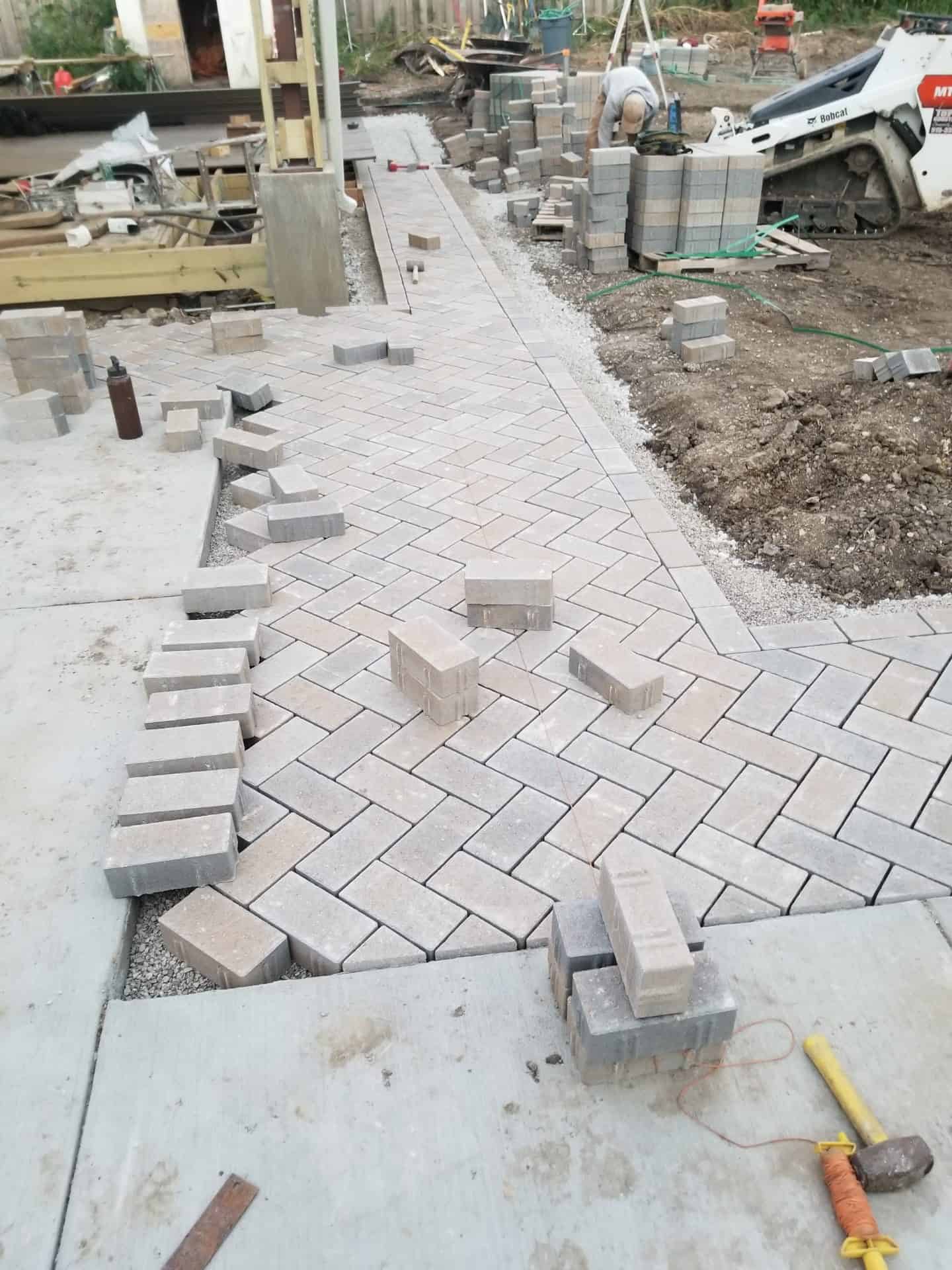 Paver walkway being laid course by course, with pavers stacked ready to set