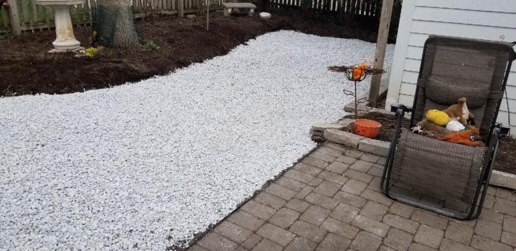 Crushed stone base spread for artificial turf beside a paver patio