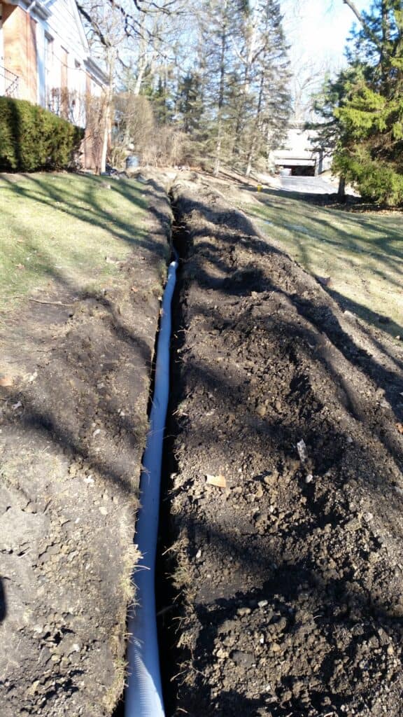 Trench with drain pipe running across a lawn from a window well