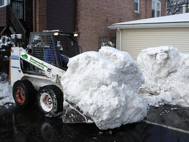 Skid steer loading large blocks of snow from a lot