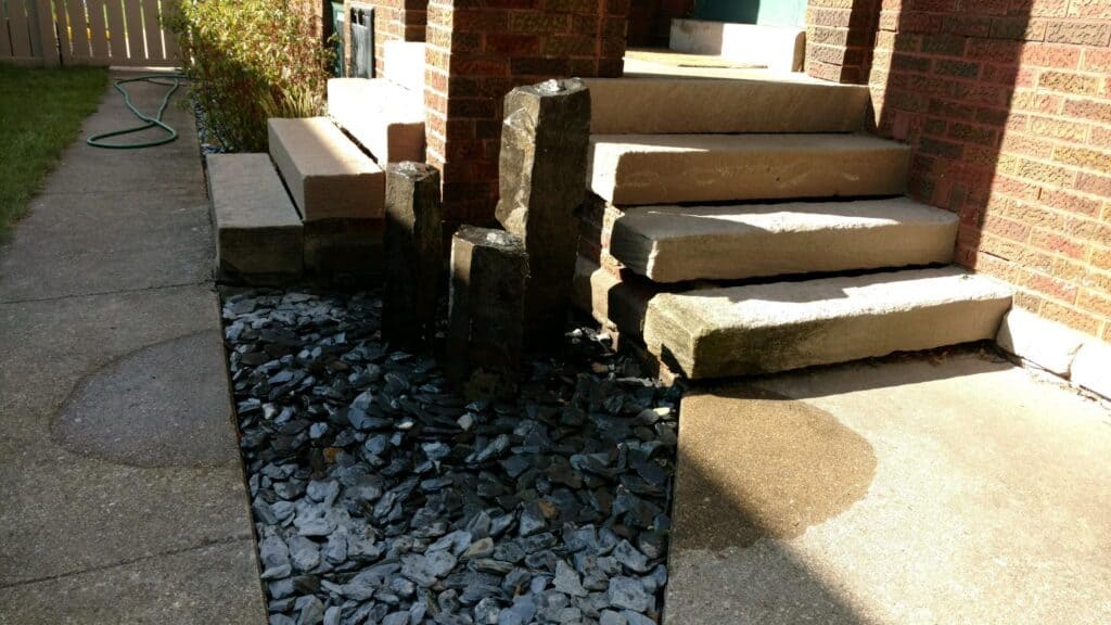 Pondless water feature of basalt columns set in slate chips beside stone steps