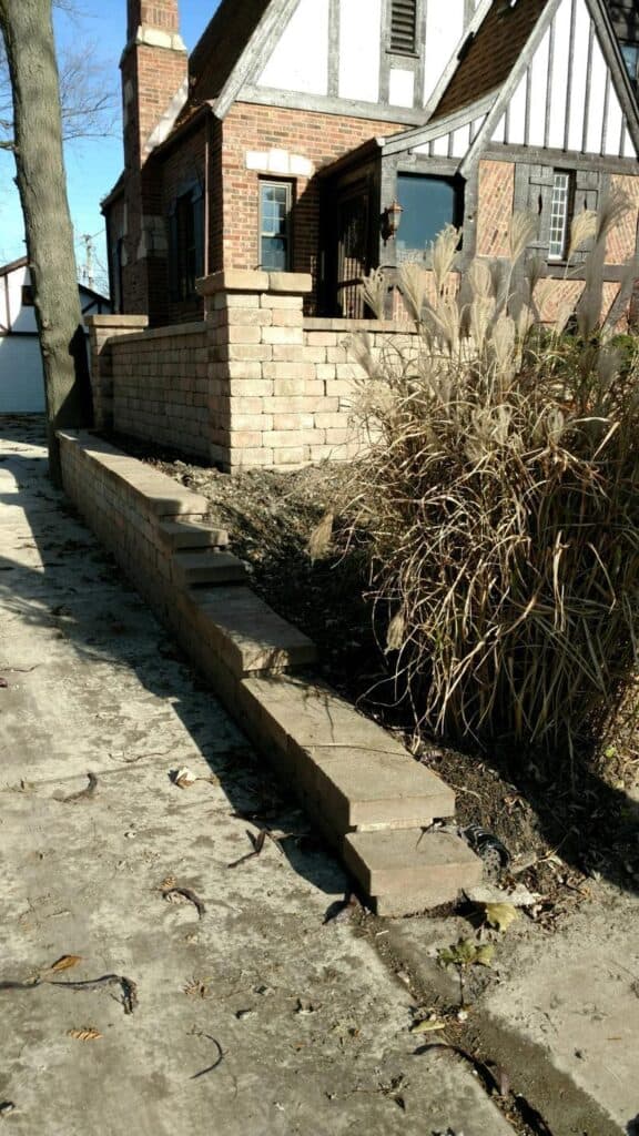 Stepped block retaining wall rebuilt along a driveway, with ornamental grasses behind it