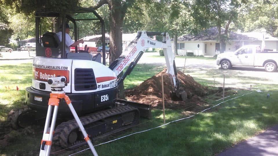 Mini excavator digging in a front yard for a new sewer pipe